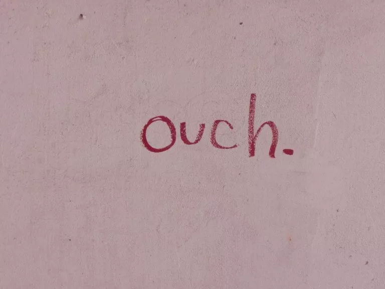 Pink wall with red text which says ouch. Text looks like it has been written in lipstick