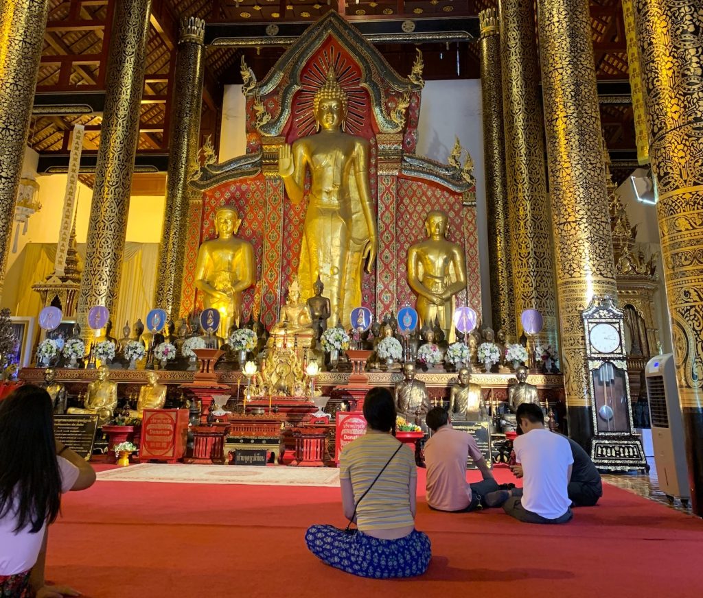 Poppy sitting cross legged in front of a large golden Buddah statue.