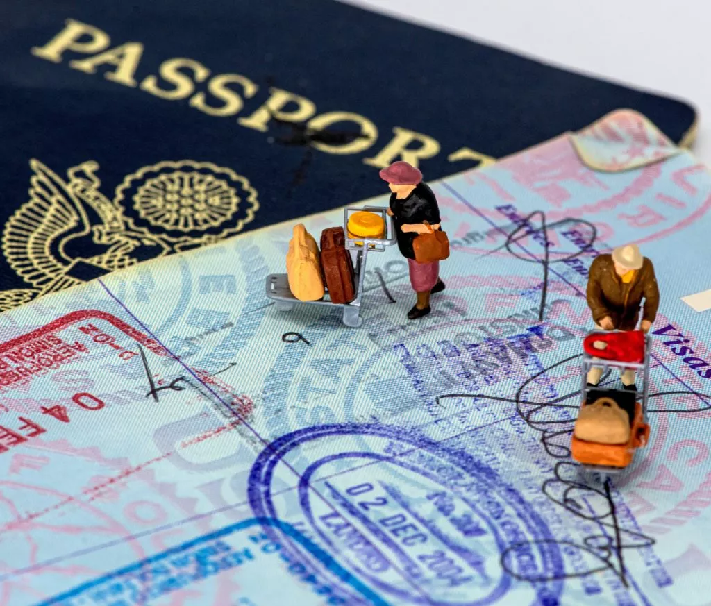 Passport with tiny figurines holding luggage stood on it